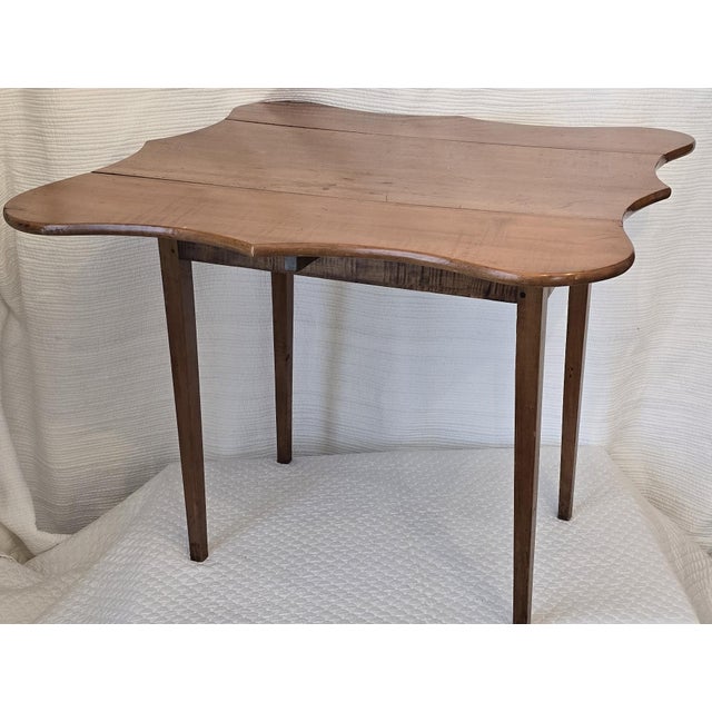 An early 19th century American tea table featuring a shaped rectangular top with two hinged drop leaves and a softly...