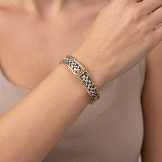 A vintage sterling silver and gold-plated cuff bracelet featuring an intricate woven design. This piece showcases a...