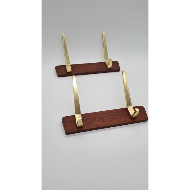 A pair of mid-century Danish wall hooks made of rosewood and brass-plated aluminum. They feature a minimalist, mid-20th-...