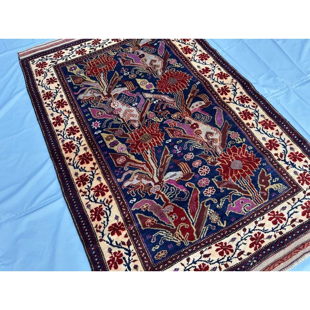 A hand-knotted Afghan rug on a deep indigo ground, worked with large serrated lotus blooms in madder red and a scattering...