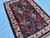A hand-knotted Afghan rug on a deep indigo ground, worked with large serrated lotus blooms in madder red and a scattering...