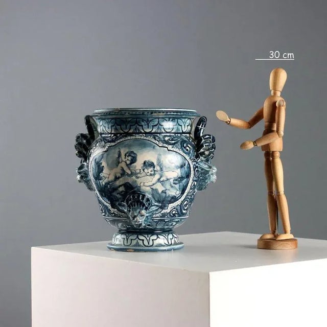 Polychrome blue majolica jug with mask-shaped handles and serpent scrolls. Decorated with cherubs and a landscape. The...