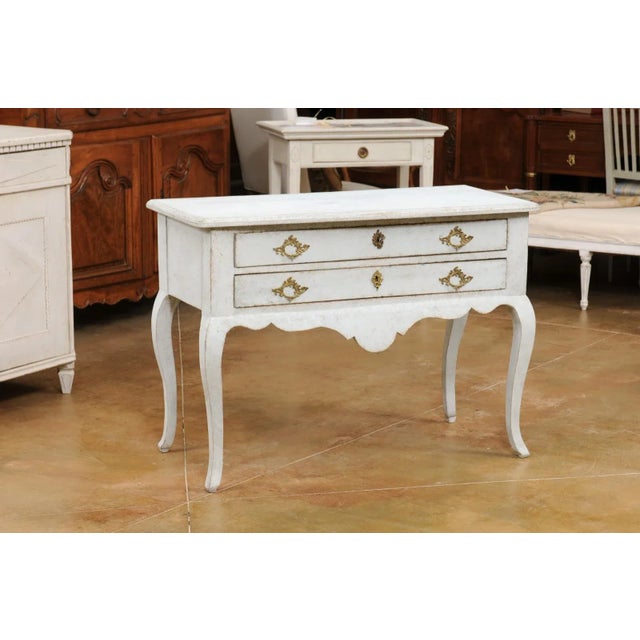 A Swedish Rococo style painted wood chest from the early 20th century, with two drawers, carved apron and cabriole legs....