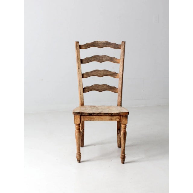 This is a vintage wooden ladder back chair. The rustic country chair features a wide seat with turned legs and a curved...
