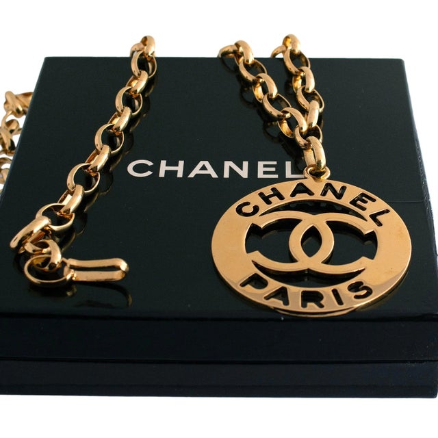 Chanel belt. The piece features a gold-plated chain with a circular disc. The disc displays the iconic interlocking "CC"...