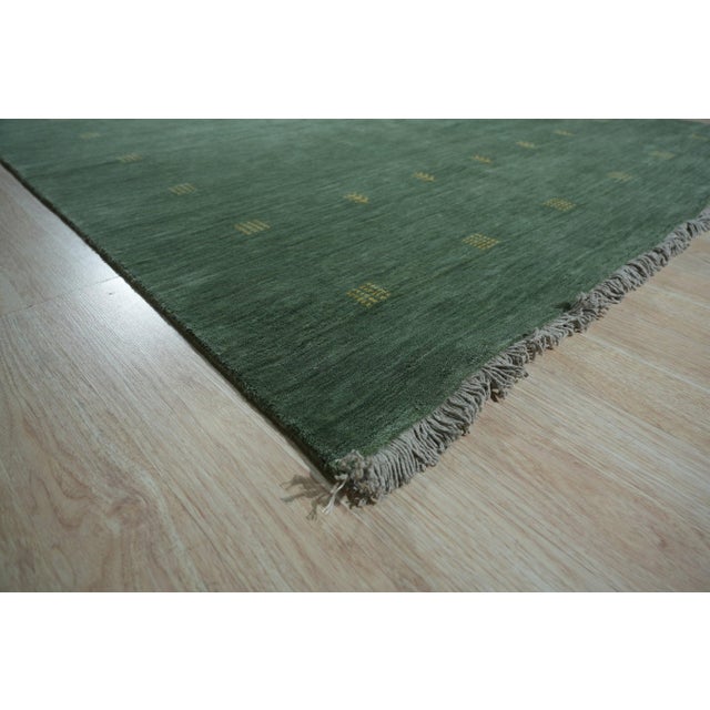 A 6' x 9' hand-knotted wool rug with a plain moss green Lori Baft (Gabbeh style) field, softly striated in tone, with...