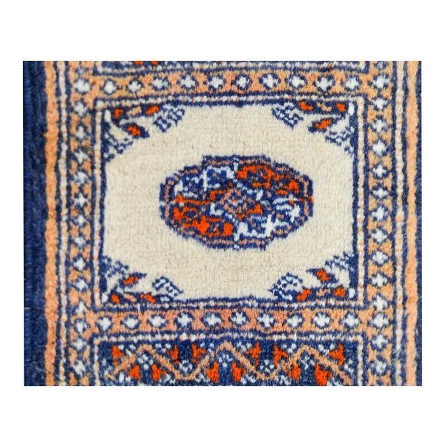 A petite vintage Pakistani Bakhara rug with a simple central medallion woven in orange and white, set against a cream...