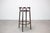 The stool features a round solid wooden seat supported by four slender legs with two circular bentwood reinforcing rings....