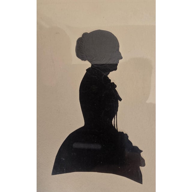 A refined pair of female profile silhouette portraits, each executed in raised black pigment on paper and presented in...