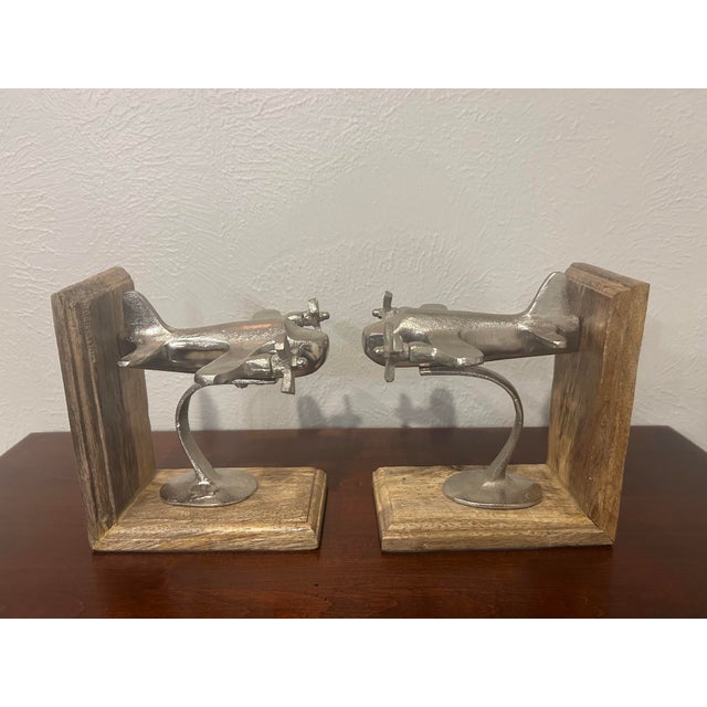 A charming pair of airplane bookends mounted on natural wood bases. Each features a propeller plane sculpture. The silver...