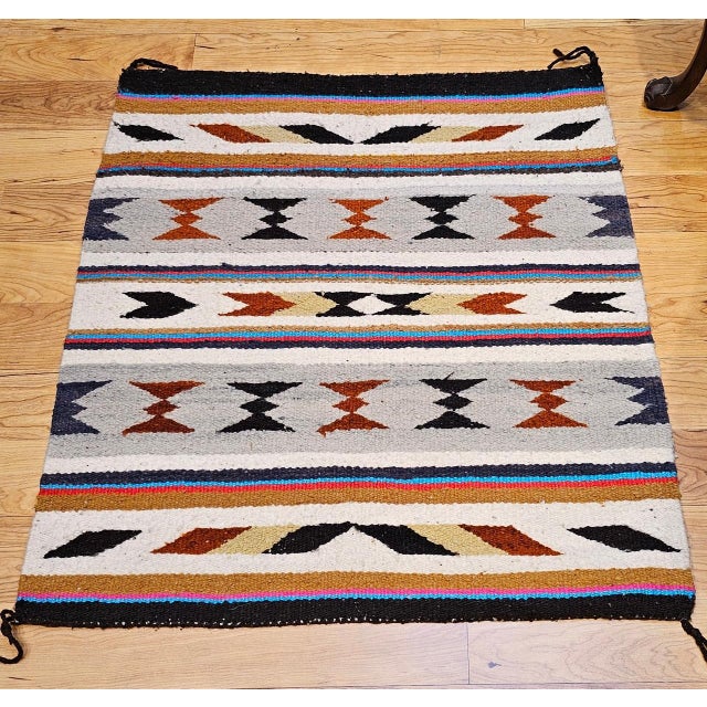 This vintage Native American Indian Navajo saddle blanket, handwoven in the third quarter of the 20th century, features a...