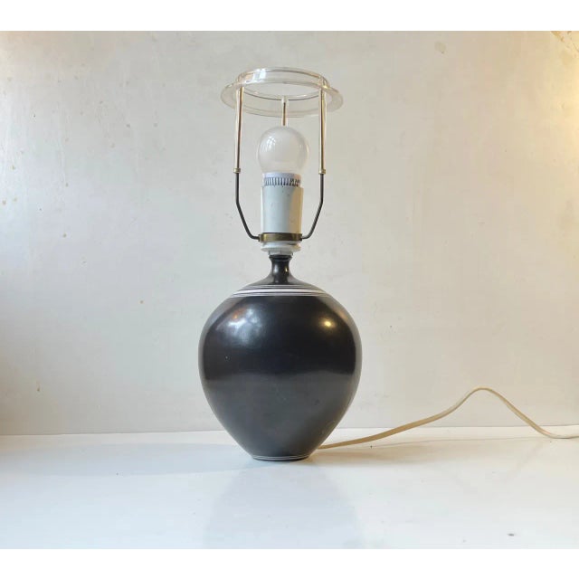 A delicately executed ceramic table lamp in black glaze with white stripes at the top and bottom. This shape is commonly...