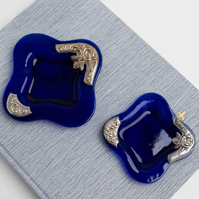 Vintage cobalt blue glass catchalls in a square silhouette, each adorned with a silver-plated floral rose motif overlay....