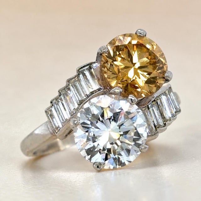 A striking platinum two-stone diamond ring featuring an exceptional pairing of colorless and fancy-colored diamonds. The...