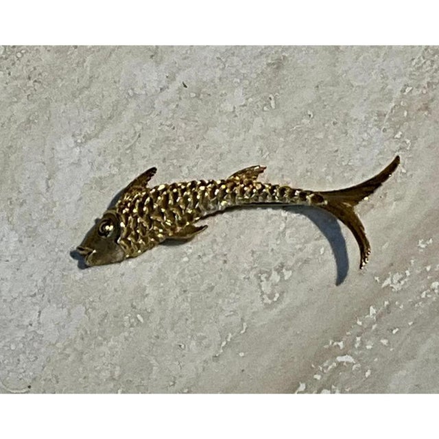 This vintage brooch is cast in gold-tone metal in the sinuous, elongated form of a leaping fish, its body curving...
