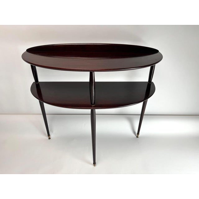 An elegant mid-century Italian console table in wood and brass. Crafted from polished dark mahogany veneer, it features a...