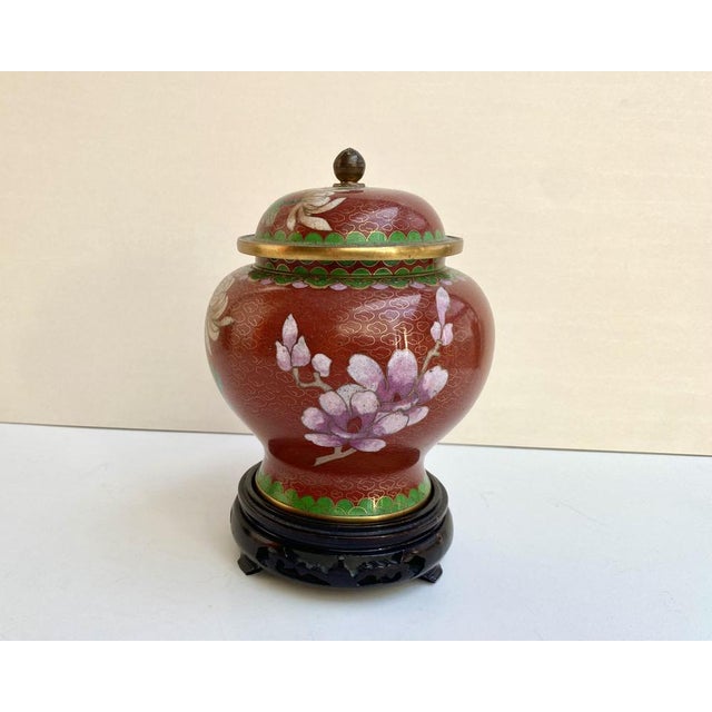 Ornate cloisonné lidded vase on wooden stand with a red background! China, 1970s. This charming jar has a floral design...