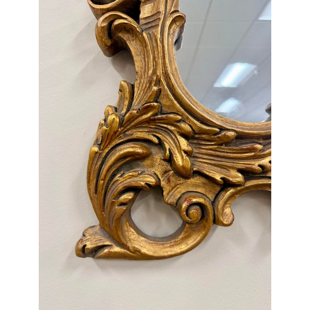 An elegant Italian Rococo-style giltwood mirror featuring an intricately hand-carved frame with flowing acanthus leaves,...
