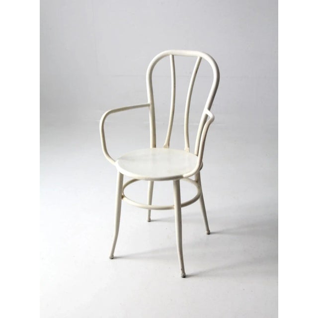 This is a mid 20th century metal bistro chair. The white arm chair has a classic curved form with round seat.