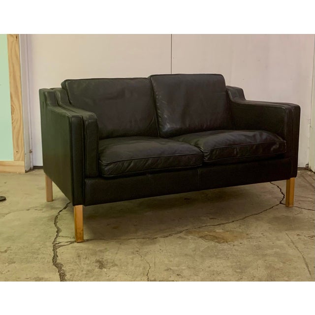 A classic Danish Modern two-seater sofa upholstered in black leather, resting on legs made from solid beech. With its...