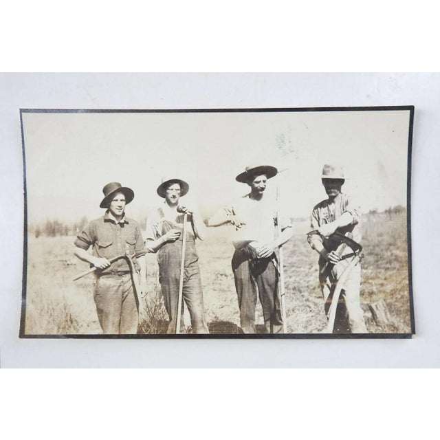 Vintage snapshot photograph. 4 hard working farm hands with rakes, scythe, shears. One fellow pouring a drink from a...