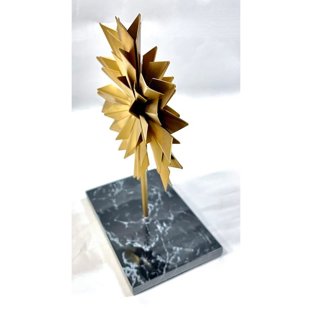 Vintage gold starburst metal table sculpture with dark blue, black, and light blue marble base. Depicts gold abstract...