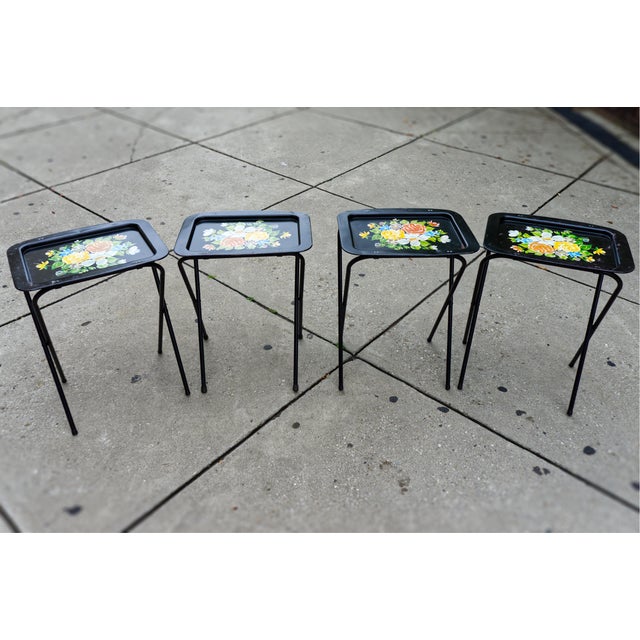 A set of four black metal folding TV dinner tray tables with floral hand painted motif.