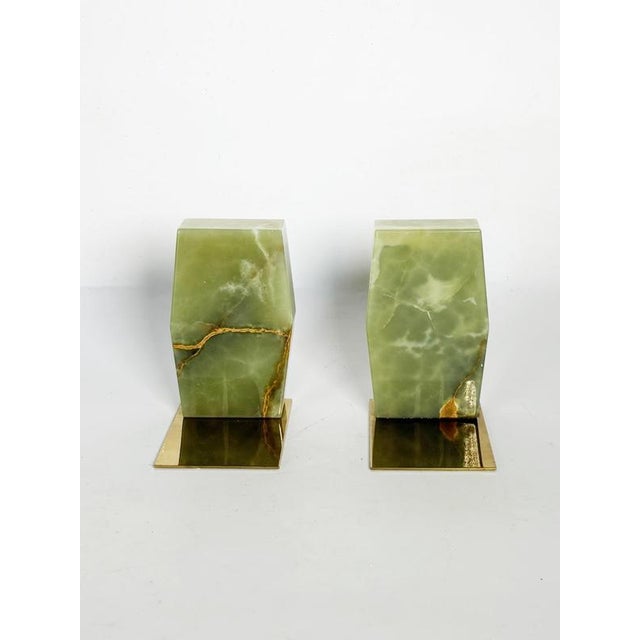 An elegant pair of bookends featuring blocks of natural green onyx set on polished brass bases. The mineral's magnificent...