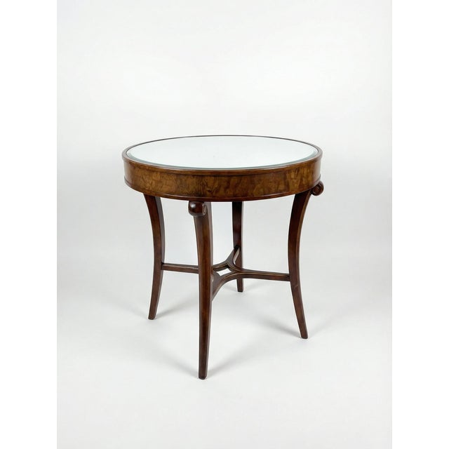 A refined and sculptural side table featuring a rich wood finish, gently curved legs, and a round mirrored top. The design...