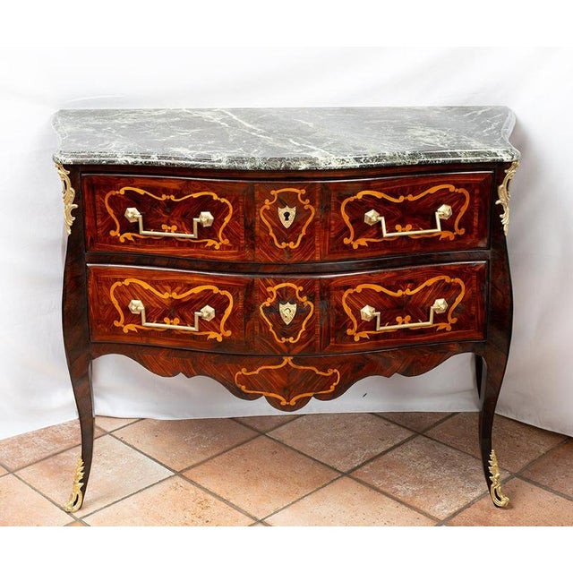 Antique French Louis XV chest of drawers crafted from fine exotic woods, featuring a marble top and gilded bronze...