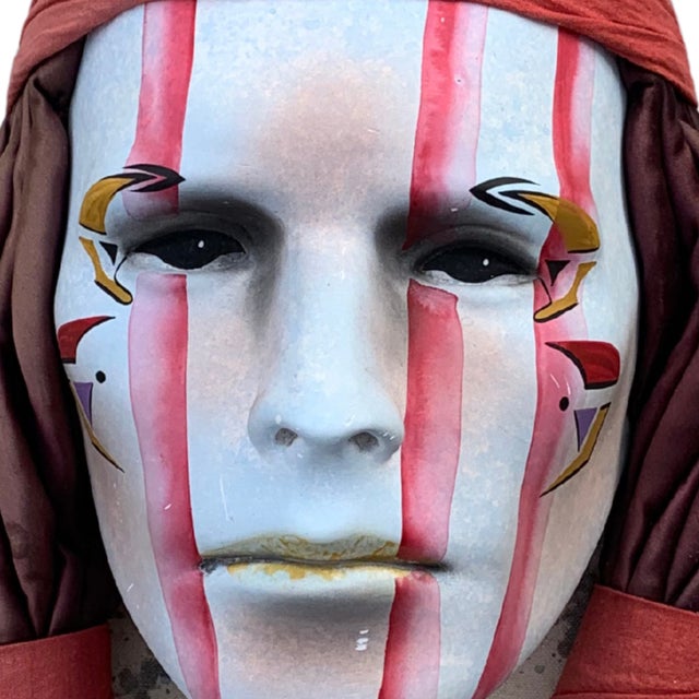 A striking ceramic wall mask by Dyan Nelson, featuring a serene, forward-facing visage adorned with hand-painted symbolic...