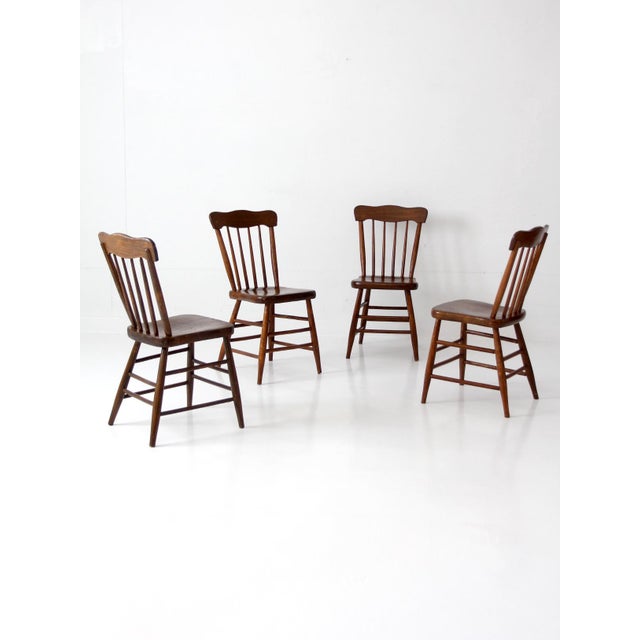 Set of four antique farmhouse chairs with plank seats, spindle backs, and gently curved crest rails. The shaped seats and...