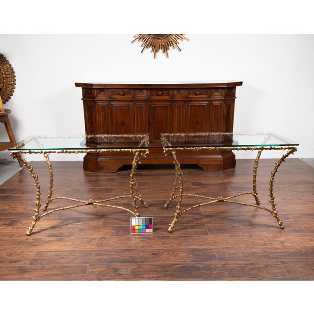 A pair of gilt bronze console tables from the mid-20th century, with faux bois motifs, glass tops and cross stretchers....