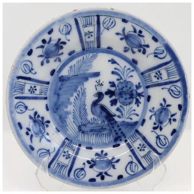 DETAILS An antique tin-glazed, pottery Delft round plate, decorated with a peacock in a Chinese style garden with a wide...