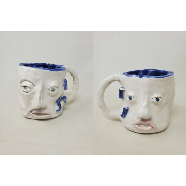 Here is a unique handcrafted decorative mug featuring two faces - a blue-eyed face on one side and a green-eyed face on...