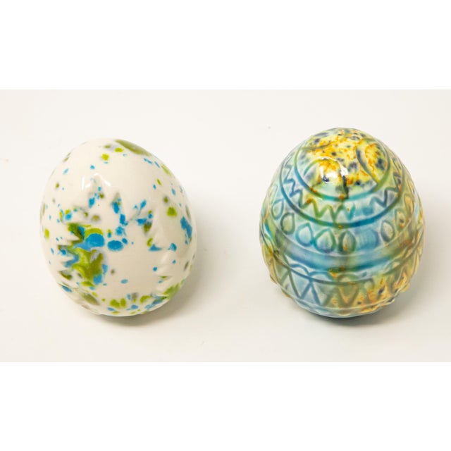 Offering a pair of ceramic glazed eggs. One egg is ivory, with blue and green spots with a tree stamped into it. The other...