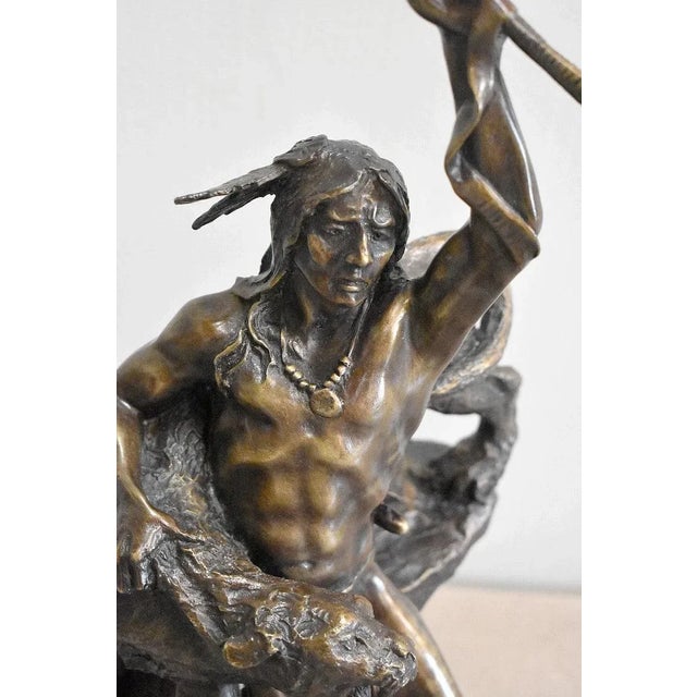 Brown patina bronze figure of an Indian warrior, holding a roaring puma under his right arm and brandishing a pipe in his...