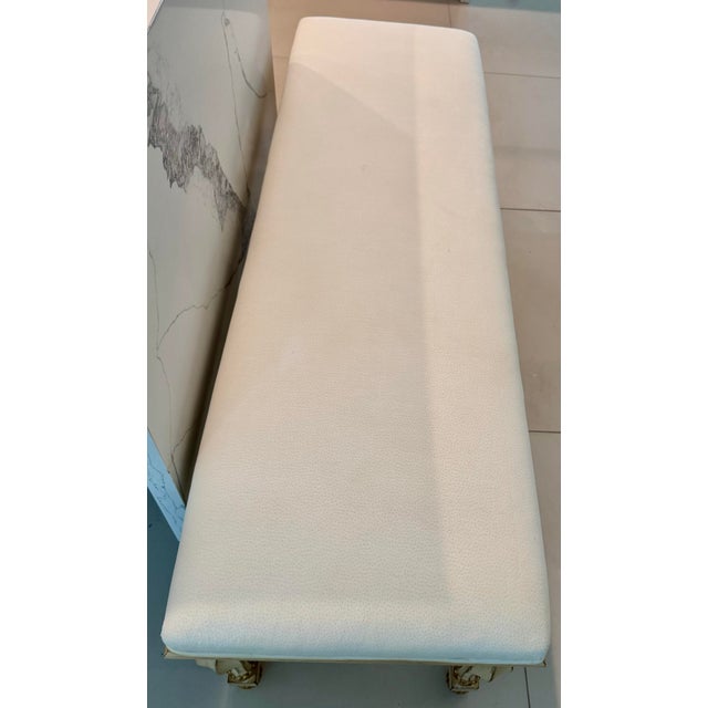 Rectangular carved wood bench with hand painted antiqued ivory finish and gold leaf accents. Bench has an upholstered...