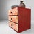 A charming Japanese tabletop drawer cabinet with three drawers, decorative floral fronts and a warm red-and-gold finish....