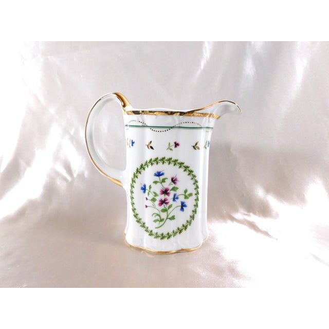 This is a white Godinger creamer in the Petit Fleur pattern. It is white with a green wreath with purple and blue flower...