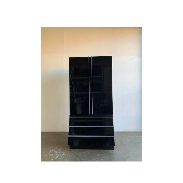 This 1980s high polish black armoire features three large drawers at the base with a angled design and open shelving on...