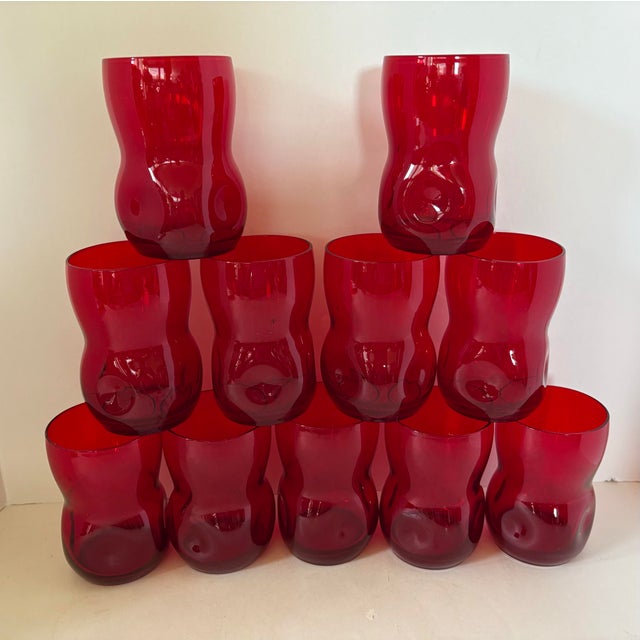 A striking set of eleven vintage ruby red art glass tumblers featuring a sculptural waisted silhouette that feels equally...