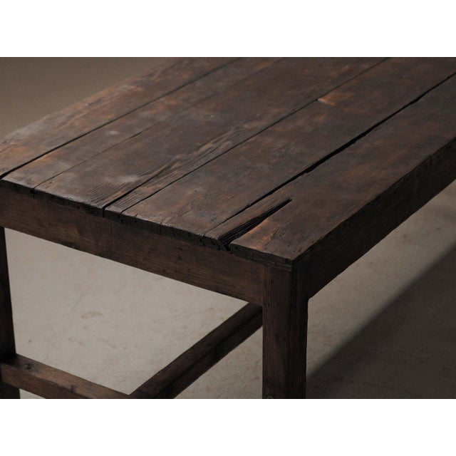 Simple and sturdy farmhouse table in solid pine, with a plank top and four straight legs joined by low stretchers. The...
