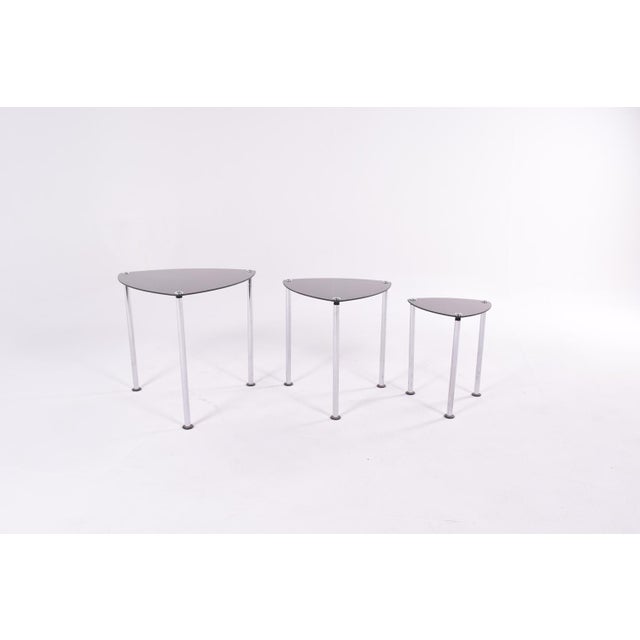 This set of triangular-shaped nesting tables features a crome-plated structure with a smoked black glass top.