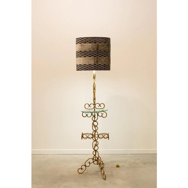 Floor lamp made of golden metal with chain structure, central oval glass table and tripod support which gives it great...