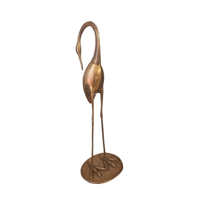 An elegant mid-century modern brass sculpture depicting a stylized crane with elongated legs and a gracefully curved neck....