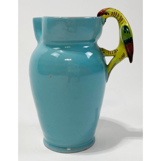 Vintage studio pottery turquoise ceramic pitcher with colorful parrot handle. Handle has shades of green, yellow and...