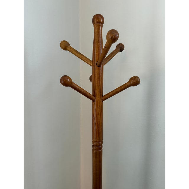 A vintage standing coat and hat rack made of honey toned wood with six angled peg arms which end in round balls. A ball...