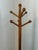 A vintage standing coat and hat rack made of honey toned wood with six angled peg arms which end in round balls. A ball...