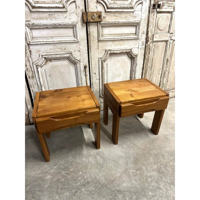Pair of elm bedside tables by maison regain, circa 1970-80. Each bedside table features a drawer with a carved handle. The...